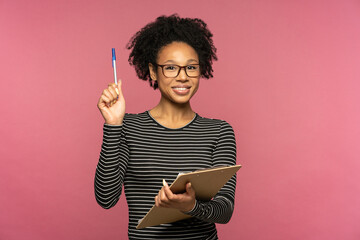Young happy Afro-American teacher woman isolated on pink studio wall. Student girl wear glasses...
