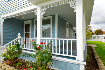 A covered wraparound porch on a vintage Victorian cottage home with rose bushes in the front in...