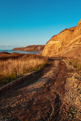 Beautiful colorful layered rock formations on sunset. Road to the sea coast. Sea on the horizon. Scenic landscape with blue sky. Natural background. Vertical view. Russia, Sakhalin Island. Copy space.