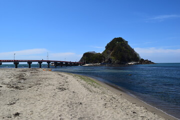 Fototapeta na wymiar 白山島（東北の江ノ島）／ 山形県鶴岡市の由良海岸沖にある白山島（はくさんじま）は、「日本の渚百選」と、「快水浴場百選」に選ばれた由良海岸のシンボル的な島で、その景観から「東北の江ノ島」と呼ばれています。由良海岸から島までは赤い白山橋が架けられており、歩いて島に渡ることが出来ます。