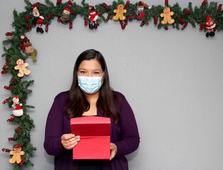 black hair latin woman with protection mask and gift box in christmas decoration, new normal...