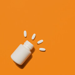 White medical pills and tablets spilling out of a plastic bottle. Medicine creative concepts. Orange background. Flat lay top view, copy space