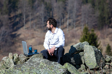hansome bearded male manager in office shirt away from home using phone and laptop at outdoor open...