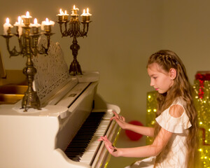 Obraz premium Little girl plays the piano by candlelight.