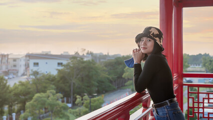 Happy young woman holding protective mask for prevention Covid-19 and relaxing on viewpoint of city at the terrace with peaceful nature scenery, looking at sunset or sunrise on horizon, copy space