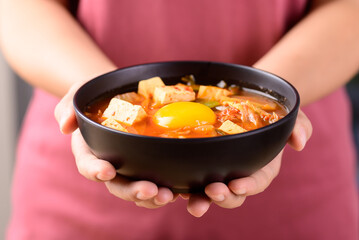 Korean food, Kimchi soup with fofu and egg in a bowl holding by hand