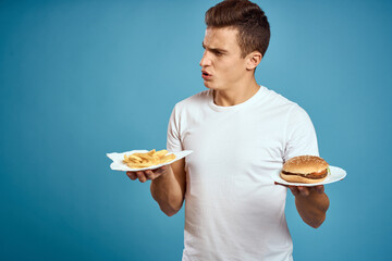 young guy with fries and hamburger on blue background interested look emotions fast food calories cropped view Copy Space