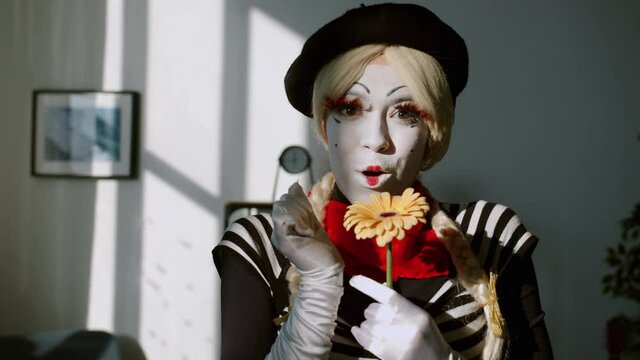 Portrait of pretty girl mime wearing funny costume and make-up smelling flower and smiling looking at camera at home. Floristly and positive emotions concept.