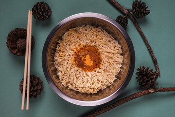 Instant noodles in a stainless steel cup arranged decorated with pine cones.