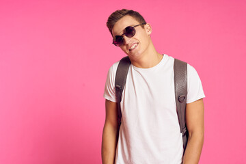 Portrait of a man in a white T-shirt and with a backpack on his back sunglasses pink background model