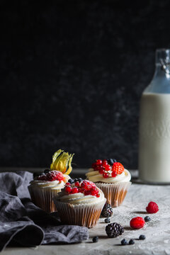 Homemade muffin next to a bottle of milk on a table and on a dark background with fresh berries around