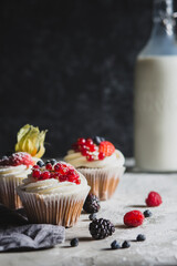 Homemade muffin next to a bottle of milk on a table and on a dark background with fresh berries around