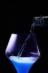 Blue drink is poured into a glass. Black background.