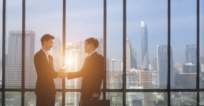Negotiating business,Image of businesswomen Handshaking. young asuan businessmen shaking hands together while standing by windows in an office