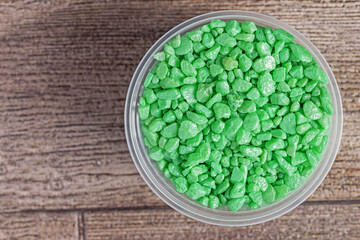 Top view of a plastic jar with decorative green stones on a wooden surface