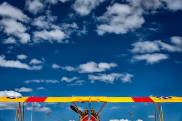 the top wing of a red and yellow biplane against a vast blue sky with clouds, symmetrical  © Randal