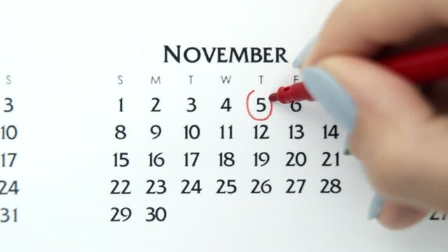 Female hand circle day in calendar date with a red marker. Business Basics Wall Calendar Planner and Organizer. November 5th