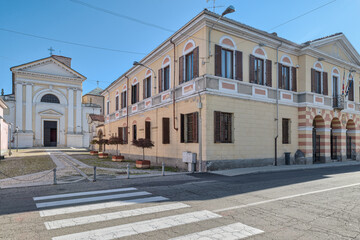 Small Italian town with the town hall and the church. Casalbeltrame town, street Vittorio Emanuele and the  parish of Santa Maria Assunta (18th century). Piedmont region