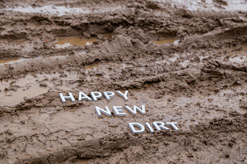 the words happy new dirt laid with silver metal letters on wet mud surface