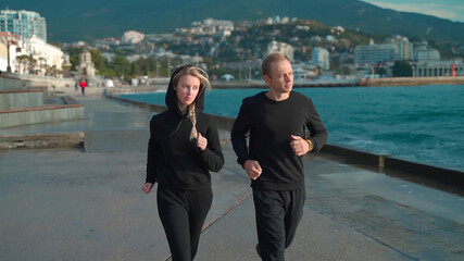 Young couple in sportswear go for a morning jog along the sea. The guy and the girl go in for sports together. They run along the sea along the embankment.