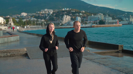 Young couple in sportswear go for a morning jog along the sea. The guy and the girl go in for sports together. They run along the sea along the embankment.