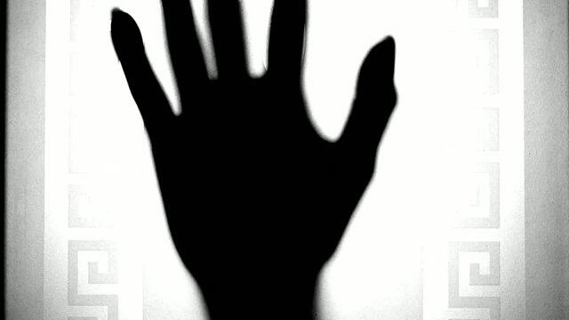 A vague female hand descends behind frosted glass. The concept of domestic violence, loneliness, horror. Blurred vintage moving