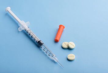 a syringe with a vaccine and pills on a blue background. syringe with antibiotic pills on a blue background.