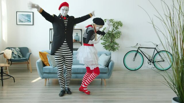 Slow motion of man and woman funny mimes dancing and having fun indoors in apartment wearing colorful clothing and make-up. People and joy concept.