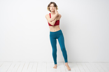 sports woman in a bright room doing yoga in full growth blue leggings and a red tank top