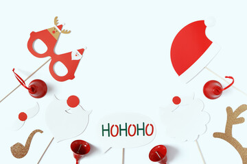 Mock up of Christmas props (a Santa Claus hat, beard or mustache, funny glasses, golden deer antlers, a smoking pipe, the phrase "hohoho") and red bells. Flat lay, top view, copy space.