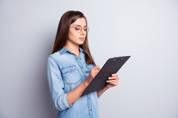 Fototapeta premium Portrait of calm concentrated lady writing on clip board eyewear pen in hand isolated on grey color background