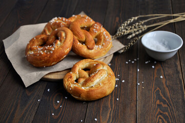 Homemade pretzels, salt and ears of wheat on a dark wooden table