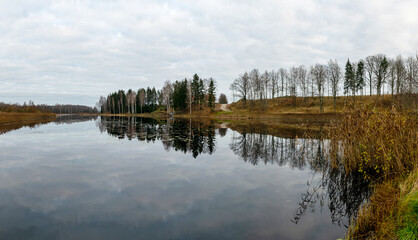 Opposite bank of lake in the autumn, cloudy sky, late autumn, bare tree silhouettes and reflections in the water