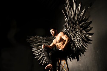 handsome athletic man in black angel costume on black background