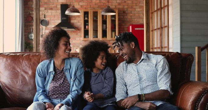 Happy African couple with little daughter doing dab gesture seated on sofa. Dabbing family having fun together at home, perform dab dance sign laughing feels carefree celebrate event, winners concept