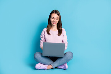 Naklejka premium Full length photo of pretty lovely student girl sitting floor crossed legs hold netbook remote communication concept wear violet pullover sneakers denim isolated blue color background