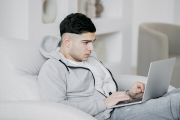 carefully reading the latest news on a laptop computer, a man in gray jeans and a jacket, a focused face. Cozy bright apartment design