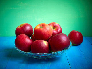 Bright red and yellow apples in a vase on a blue background.
