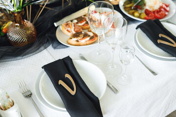 Close up of festive table setting with wine glasses, food and black napkins