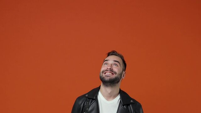 Excited surprised amazed young bearded man 20s wearing casual black leather jacket posing isolated on orange color background in studio. People emotions lifestyle concept. Pointing index fingers up