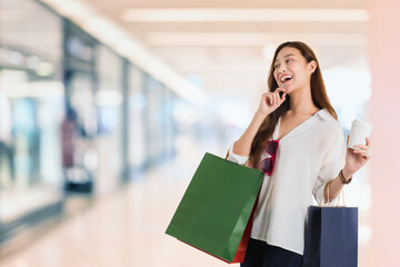 Asian beautiful women blogger shopping and hand pointing with a shopping bag in blurred shopping mall interior background.Concept of online shopping business.