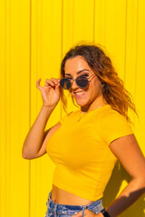 Lifestyle, Caucasian blonde girl in yellow shirts on a yellow background. Fashionable posing putting on the gorgeous sunglasses with a smile