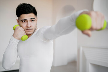 training with dumbbells in his hands, preparing for cardio training athlete at home during the pandemic, looking forward. young man athletic body in comfortable sportswear.