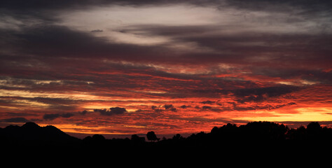 Hills and treeline silhouettes against amazing colorful sunset sky