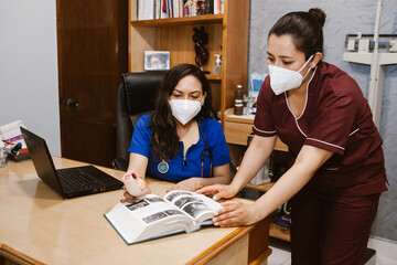 Latin doctor consulting handbook at her office - obrazy, fototapety, plakaty