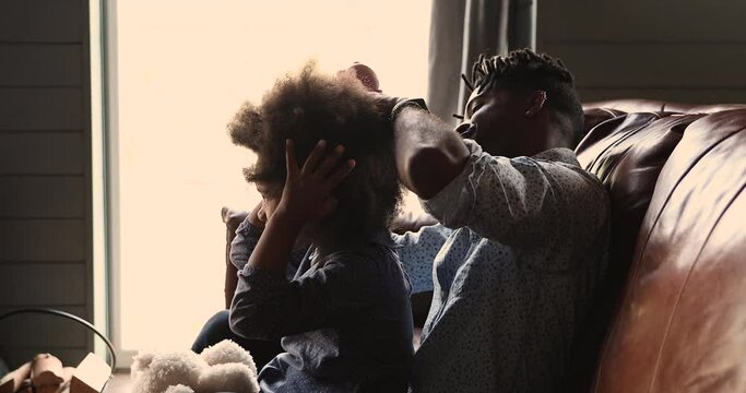 Side view loving mixed race dad help child with hairstyle brushing little daughters curly afro short hair while sit on couch. Communication, morning routine, love and care, happy fatherhood concept
