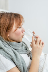 diseased girl sitting on a bed and drinking water from a glass at home
