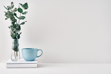 A mug, a stack of books, a wooden board and a transparent vase with eucalyptus branches. Eco-friendly materials in interior decor, minimalism. Copy space, mock up