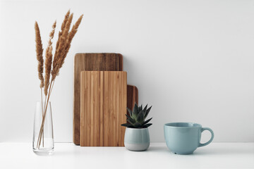 A mug, a potted houseplant, a clear vase and a wooden cutting board. Eco-friendly materials in the decor of the room, minimalism. Copy space, mock up.
