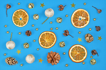 Seasonal Christmas flat lay with dried orange slices, fir cones, tree ornament baubles and golden bells on blue background